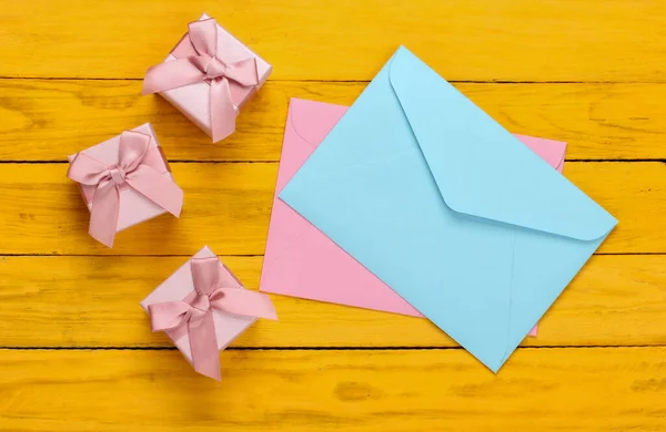 Envelope with gift boxes on yellow wooden background. Top view