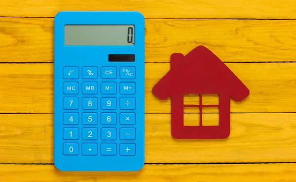 Calculation of cost or rental housing. Calculator with a house figure on yellow wooden background.