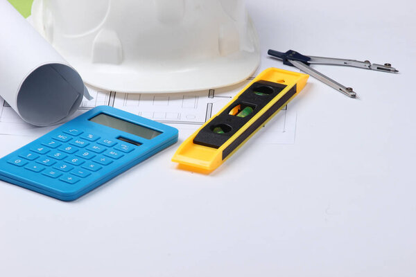 Hard hat with building level, calculator, compass, blueprint on white studio background. Engineering, construction equipment.