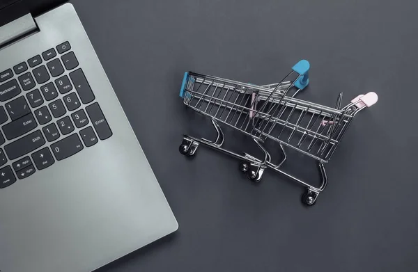 Online shopping. Laptop with supermarket trolleys on gray background. Top view. Flat lay