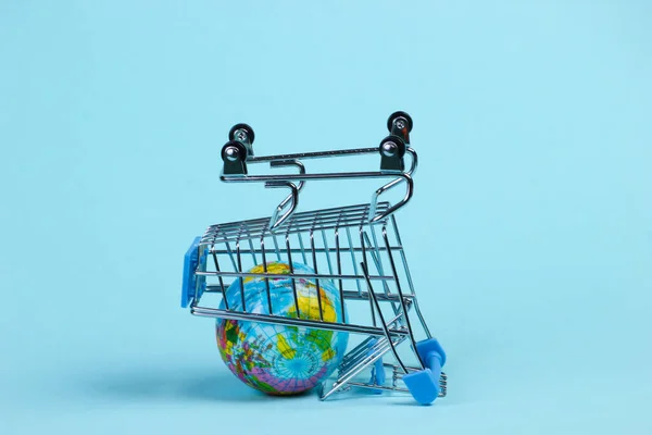 全球购物概念 带有蓝色工作室背景的地球仪超级市场推车 最低限度主义 — 图库照片