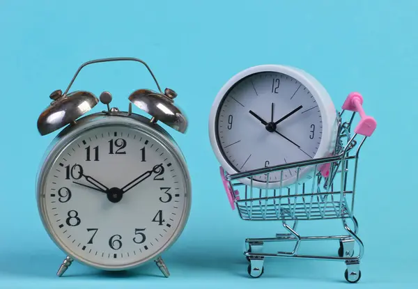 買い物の時間だ 青い背景に目覚まし時計とスーパーマーケットトロリー — ストック写真