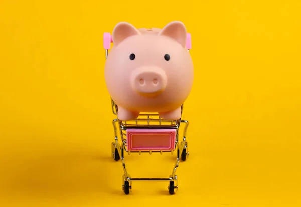 Shopping trolley with piggy bank close-up on yellow background