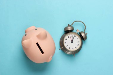 Mavi arka planda domuzcuk kumbarası ve eski alarm saati. Minimalist stüdyo çekimi. Genel bakış. Düz yatıyordu.