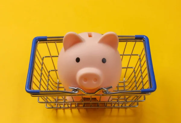 Supermarket basket with piggy bank on a yellow background. Shopping concept