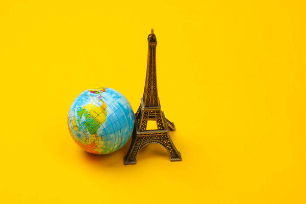 Минимализм путешествует натюрмортом. Фигура Эйфелевой башни, земной шар на желтом фоне.
