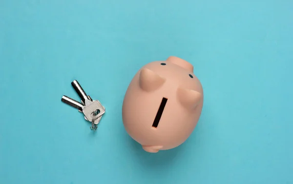 Piggy bank with house keys on a blue background. Payment of rent for housing, save money for house. Top view