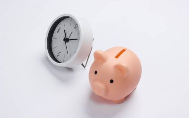 Para kazanma zamanı. Depozito. Beyaz arka planda beyaz saat ve kumbara. Minimalist stüdyo çekimi.