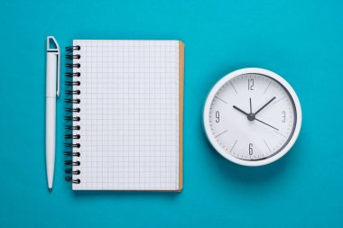 Mavi arka planda beyaz saat ve defter. Minimalist stüdyo çekimi. Üst görünüm