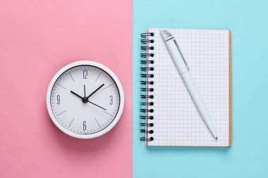 Pembe pastel arka planda beyaz saat ve defter. Minimalist stüdyo çekimi. Üst görünüm