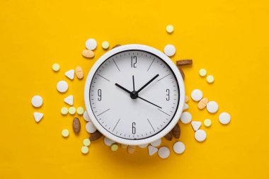 İlaç alma zamanı. Sarı arka planda hapları olan beyaz saat. Üst Manzara. Düz yatıyordu