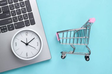 İnternetten alışveriş zamanı. Mavi arka planda saat ve süpermarket tramvayı olan bilgisayar klavyesi. Üst görünüm