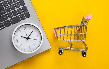 İnternetten alışveriş zamanı. Sarı arka planda saat ve süpermarket tramvayı olan bilgisayar klavyesi. Üst görünüm