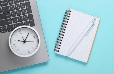 Mavi arka planda dizüstü bilgisayar, defter ve çalar saat. Zaman geçiyor. İş ve taahhütlerde acil teslim tarihi kavramı.