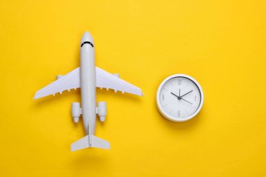 Seyahat zamanı. Sarı arka planda uçak heykelciği ve saat. Üst görünüm