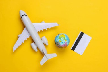 Seyahat teması. Küreye sahip bir uçak, sarı arka planda kredi kartı. Üst manzara, düz uzanma