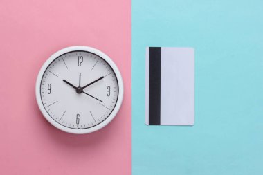 Mavi-pembe pastel arka planda kredi kartı olan beyaz saat. Üst görünüm