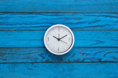 Mavi ahşap arka planda beyaz saat. Zaman geçiyor. Üst görünüm