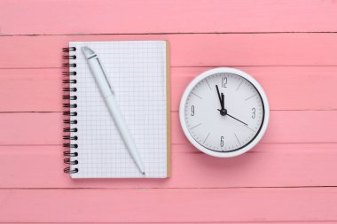 Pembe ahşap arka planda beyaz saat ve defter. Minimalist stüdyo çekimi. Üst görünüm