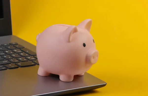 Piggy bank on laptop keyboard. Yellow studio background. Make money online or internet business
