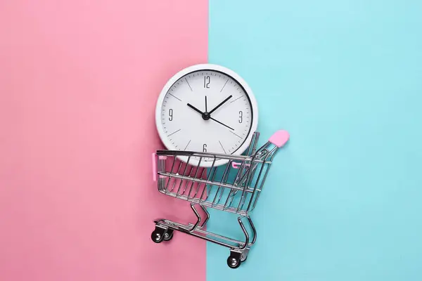 购物时间 超级市场有钟的手推车 粉色蓝色背景 简约主义顶部视图 — 图库照片