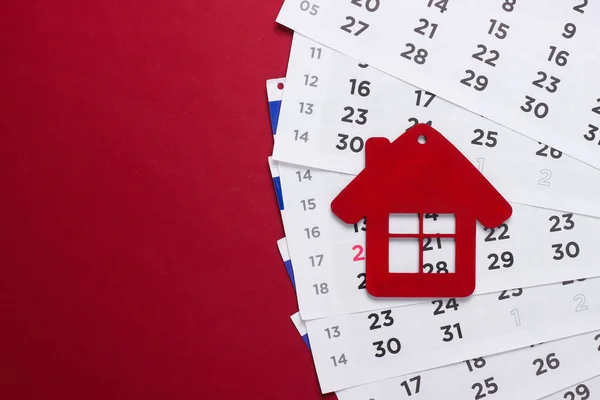 Payment of rent for housing. Figurine of a house with a monthly calendar on a red background.