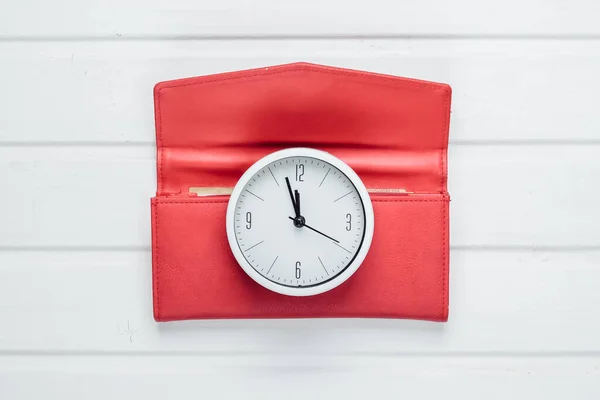 Time to make money. White clock and red wallet on white wooden background. Minimalistic studio shot. Top view