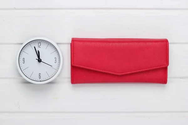 Time to make money. White clock and red wallet on white wooden background. Minimalistic studio shot. Top view