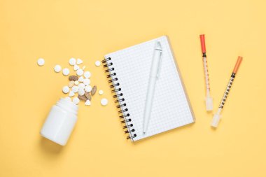 Tıbbi tema. Şırıngalar ve defter, sarı arka planda haplar. Üst görünüm