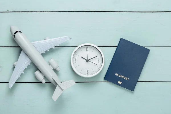 Time to travel. Plane figurine and clock, passport on blue wooden background. Top view. Flat lay