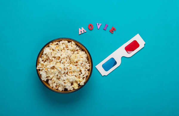 Movie time. Stereoscopic anaglyph disposable paper 3d glasses and popcorn on blue background. Top view