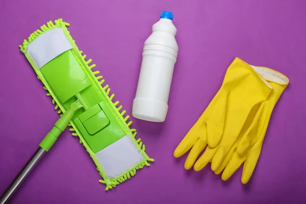 Cleaning products. Plastic green mop, gloves, bottle of detergent on purple background. Disinfection and cleaning in the house. Top view