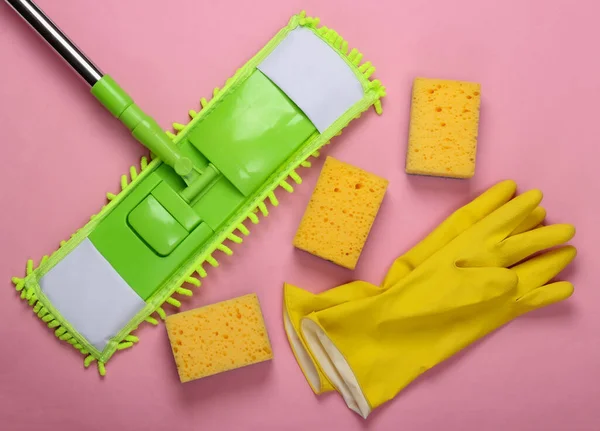 Cleaning products. Plastic green mop, gloves and sponges on pink background. Disinfection and cleaning in the house. Top view