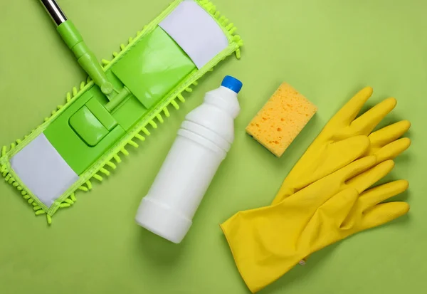 Cleaning products. Plastic mop, gloves, bottle of detergent, sponge on green background. Disinfection and cleaning in the house. Top view