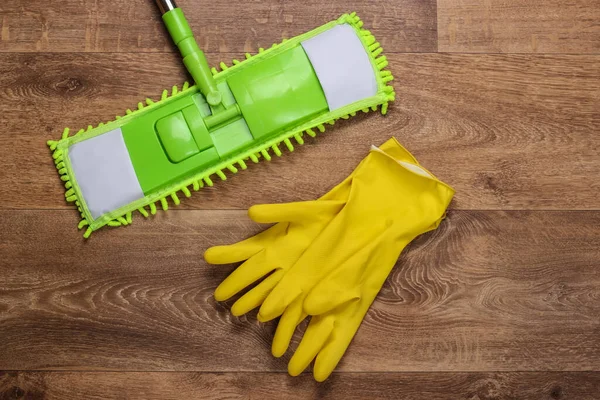 stock image Plastic green mop, gloves on wooden floor. Disinfection and cleaning in the house. Top view