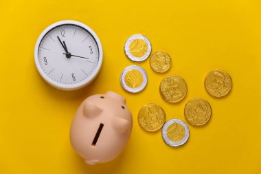 Vakit nakittir. Kumbaralı beyaz saat ve sarı arka planda bozuk paralar. Üst görünüm