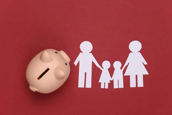 Paper happy family together with piggy bank on red background. Family budget