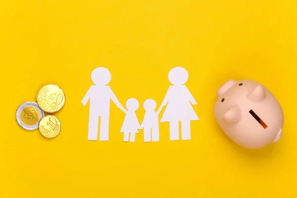 Paper happy family together with piggy bank, coins on yellow background. Family budget