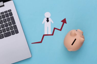 Dizüstü bilgisayar, domuz kumbarası ve büyüme okunda kağıt adam. Mavi arka plan. Finansal ve sosyal başarının sembolü, ilerlemeye giden merdiven. Kariyer basamağı.