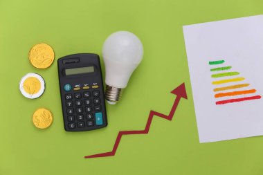 Enerji tüketimini hesaplama, modernleştirme kavramı. Enerji sınıfı, yeşil arkaplanda ampul, sikke ve hesap makinesi ile ilgilenen büyüme oku