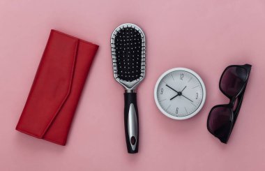 Kadın aksesuarları. Cüzdan, tarak, güneş gözlüğü ve pembe arka planda saat. Üst görünüm.