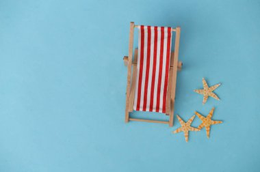 Çizgili plaj koltuğu ve mavi arka planda deniz yıldızı. Plaj tatili, tatil köyü sembolü. Rahatla, yaz asgari konsepti. Üst görünüm