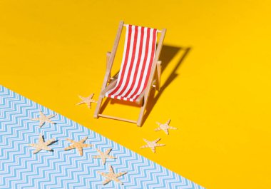 Mini plaj sandalyesi ve sarı mavi arka planda gölgeli denizyıldızı. Güneş ışığı. Plaj tatili, tatil köyü sembolü. Rahatla, yaz asgari konsepti.