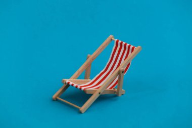 Mavi arka planda çizgili bir plaj sandalyesi. Plaj tatili, tatil köyü sembolü. Rahatla, yaz asgari konsepti