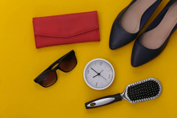 Women\'s accessories. High-heeled shoes, wallet, comb, sunglasses and clock on yellow background. Top view.