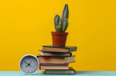 Kaktüslü kitap yığını ve sarı zemin üzerindeki saat