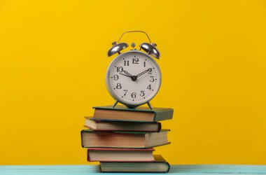 Bir yığın kitabın üzerindeki çalar saat. Sarı arkaplan