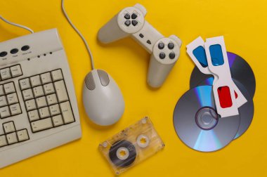 Retro eğlence. Eski moda klavye, bilgisayar faresi, CD 'ler, oyun platformu, anaglyph gözlükleri, sarı arka planda ses kaseti. Üst Manzara. Düz yatıyordu