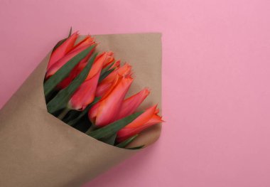 Pembe arka planda kağıt ambalajlı kırmızı lale buketi. Üst görünüm