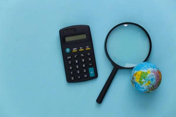 Travel concept. Magnifier with globe and calculator on a blue background. Top view. Flat lay